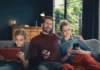FRITZ!Box: Vodafone bringt Wi-Fi 7 ins Kabelnetz Vater, Mutter und Sohn sitzen auf einem Sofa und nutzen ein Tablet, eine Fernbedienung sowie ein Smartphone