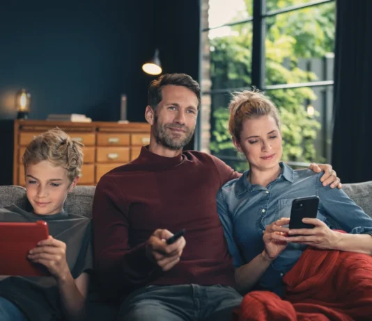 FRITZ!Box: Vodafone bringt Wi-Fi 7 ins Kabelnetz Vater, Mutter und Sohn sitzen auf einem Sofa und nutzen ein Tablet, eine Fernbedienung sowie ein Smartphone
